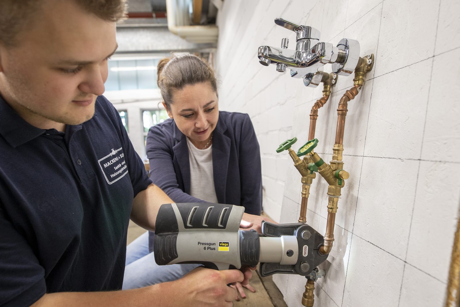 Ausbildung bei Mackens + Sohn: Auszubildender arbeitet mit der Pressmaschine, Geschäftsführerin Alina Mackens schaut zu